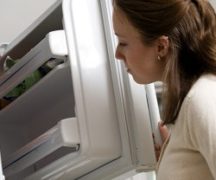 Девушка смотрит в морозильную камеру